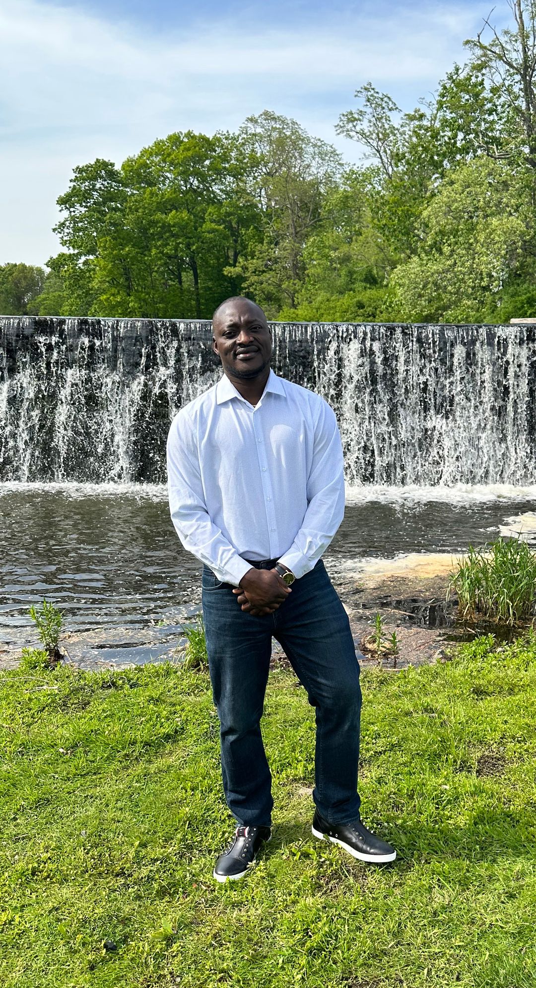 Larry Sanni standing on green grass with waterfall and trees in background